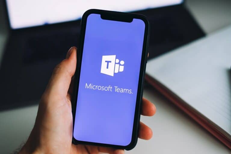 Microsoft Teams logo on a smartphone, with a hand holding the phone