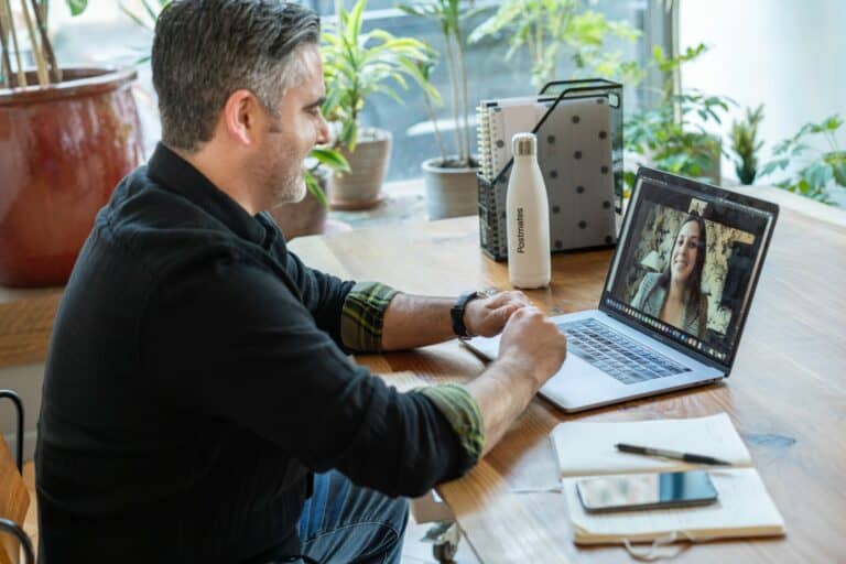 Man sitting at wooden desk with a laptop on a video call